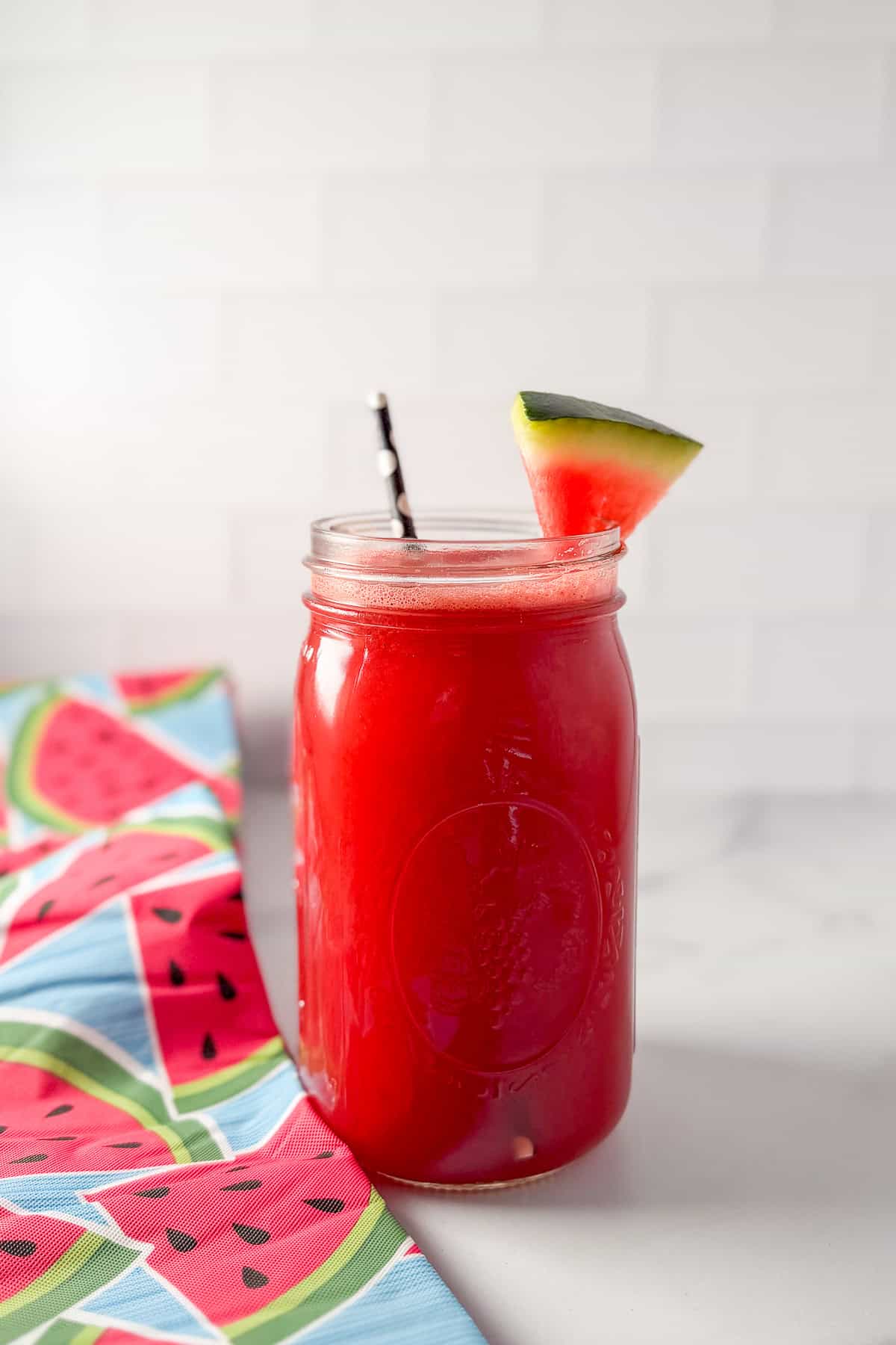 Watermelon cucumber juice in a large mason jar with  watermelon wedge and straw.
