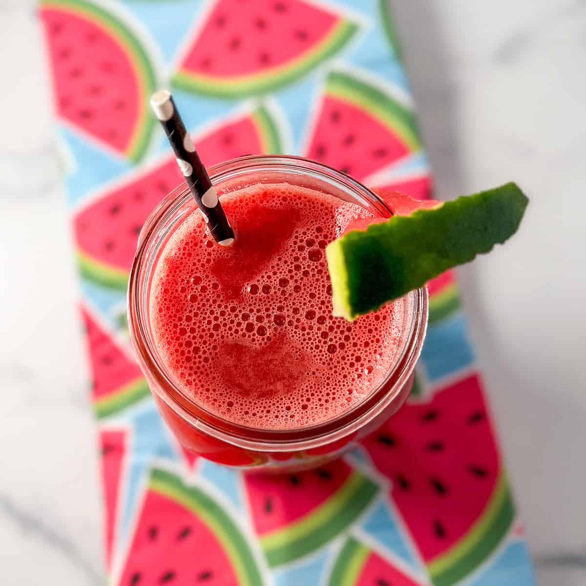 Watermelon cucumber lime juice in a mason jar with straw and melon wedge on the rim.