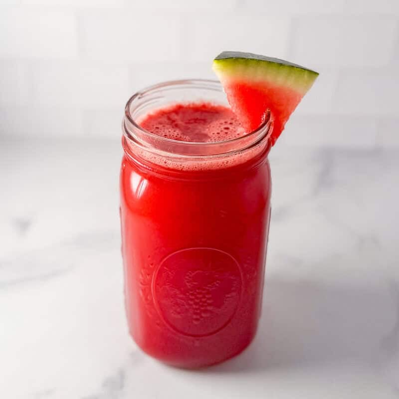 Watermelon cucumber juice in a mason jar glass with a slice of watermelon on the rim of the glass.