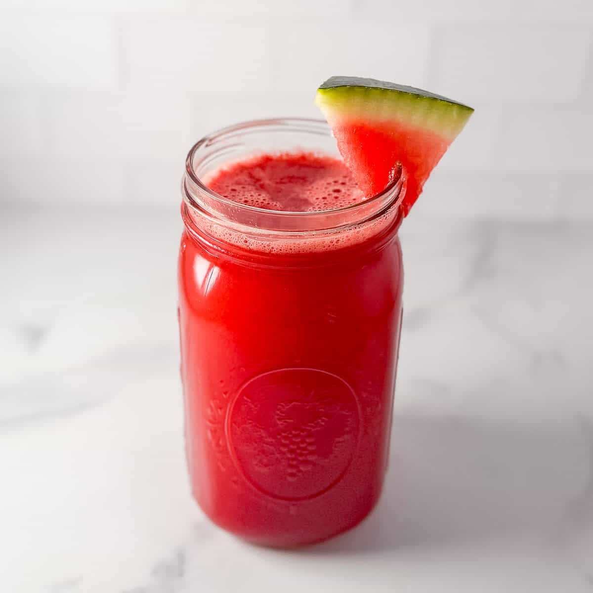 Watermelon cucumber juice in a mason jar glass with a slice of watermelon on the rim of the glass.