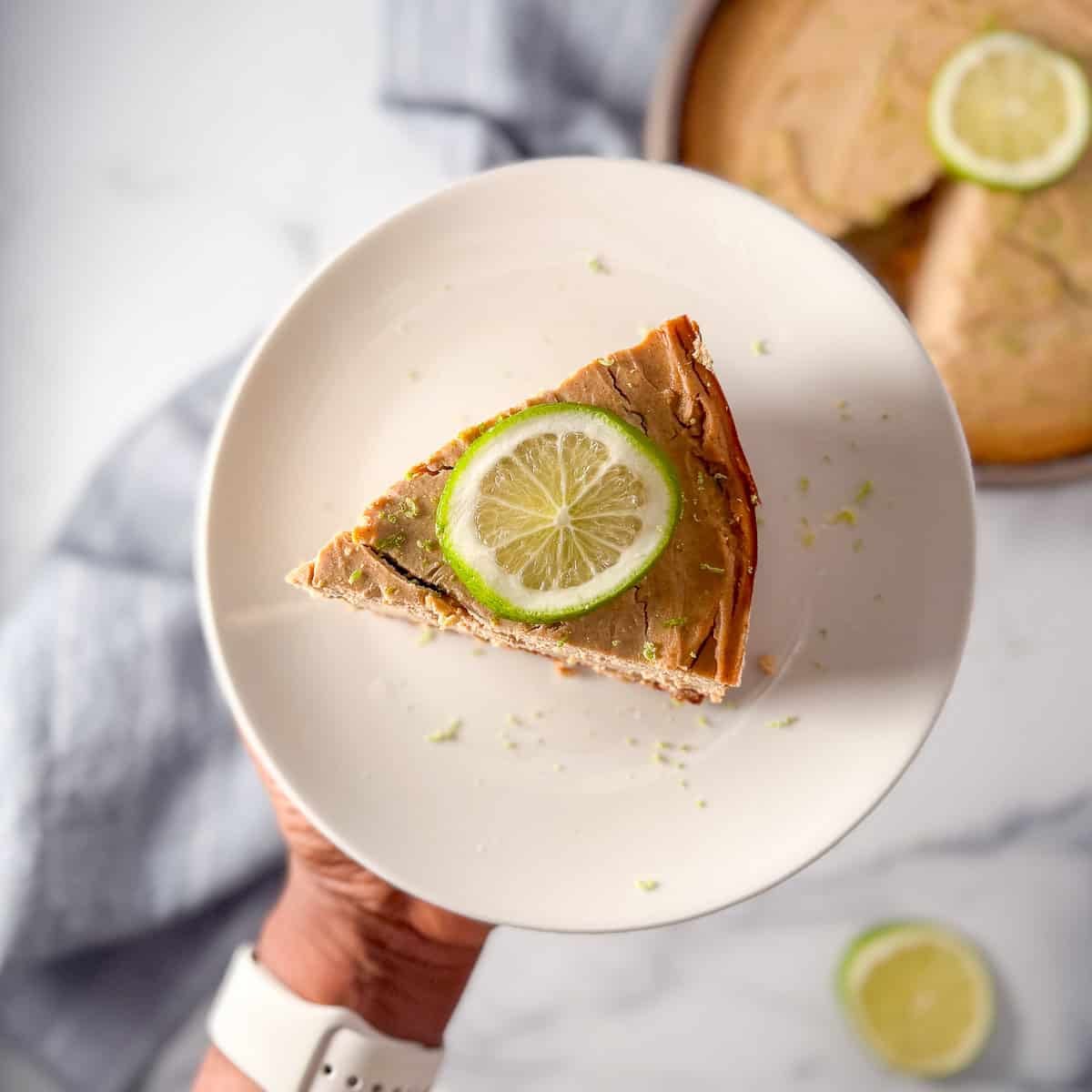 A woman's hand holding up a slice of vegan lime pie on a plate.