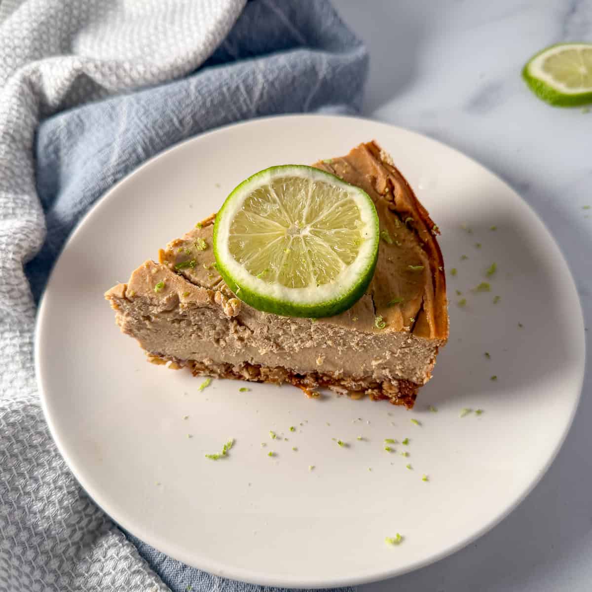 A slice of vegan lime pie on a plate with a piece of sliced lime on top.