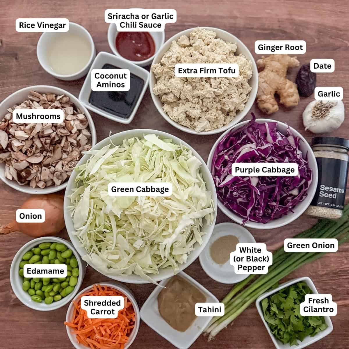 Ingredients for vegan egg roll in a bowl: cabbage, mushrooms, onion, carrots, tofu, shelled edamame, ginger, garlic, green onion, tahini, rice vinegar, coconut aminos, sriracha, and other seasonings.