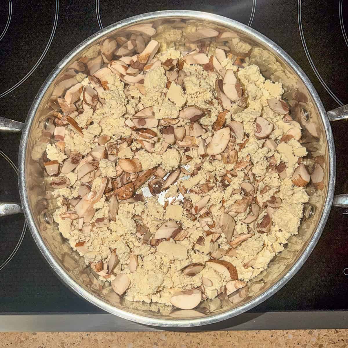 Crumbled tofu and mushrooms sautéing in a skillet.