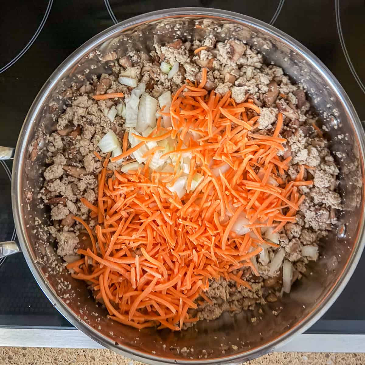 A skillet with tofu, mushrooms, onions and shredded carrots.